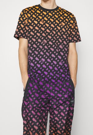 Homme portant un T-shirt à manches courtes et un pantalon assortis avec un motif en treillis noir et des couleurs dégradées allant de l'orange au violet.