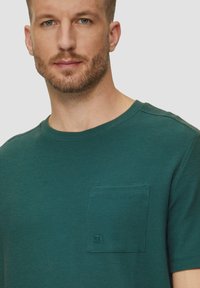 Grünes Kurzarm-T-Shirt mit Rundhalsausschnitt aus strukturiertem Stoff, mit einer Brusttasche und aufgesticktem Logo-Detail.