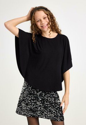 Black loose-fitting top with wide sleeves paired with a sparkling black and silver sequined skirt. Features curly hair and a headband.