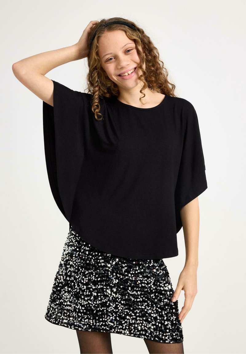 Black loose-fitting top with wide sleeves paired with a sparkling black and silver sequined skirt. Features curly hair and a headband.