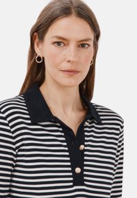 Gestreepte poloshirt met zwarte kraag, drie gouden knopen en een zachte textuur. Beschikt over dunne zwart-witte horizontale strepen.
