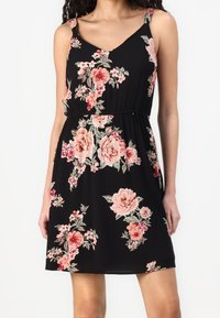 Black floral dress with spaghetti straps. Features pink and coral flower patterns, gathered waist, and a relaxed fit. Lightweight fabric with natural texture.