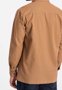 Brązowa koszula z długim rękawem wykonana z bawełny, z kołnierzykiem, mankietami na guziki i zaokrąglonym dołem. Gładka tekstura z minimalistycznym wzorem.