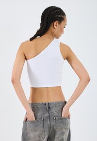 White, ribbed crop top with an asymmetrical design, featuring one shoulder strap. Pair of gray jeans with two back pockets.