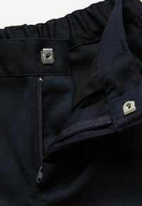 Sorte bukser i stof med lynlås og knaplukning. Har en glat tekstur og elastisk linning for komfort.