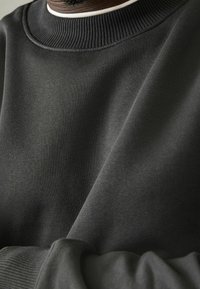 Sudadera gris oscuro con un cuello redondo de canalé y tejido texturizado. Superficie suave con un acento blanco en contraste debajo del cuello.