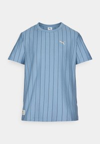 Lichtblauwe t-shirt met korte mouwen, verticale zwarte strepen, ronde halslijn en een klein gouden logo op de bovenste linkerkant van de borst. Zachte stof.