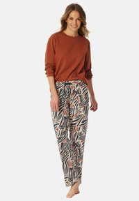 Rode longsleeve top met opgerolde mouwen, gecombineerd met crèmekleurige, gemusterde broeken met groene, oranje en zwarte abstracte ontwerpen.