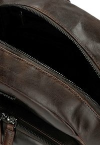 Interno di uno zaino in pelle marrone con rivestimento in tessuto nero visibile. Presenta una chiusura con zip prominente e una superficie in pelle testurizzata.