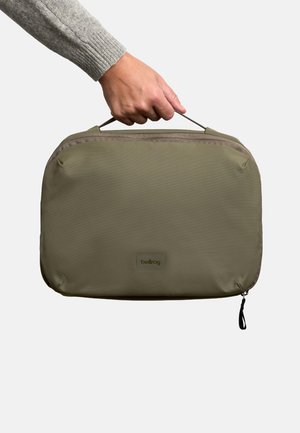 Custodia con cerniera verde oliva con trama di tessuto liscia, dotata di maniglia superiore e toppa con logo, dimensioni circa 30 x 20 x 5 cm.