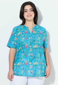 Blusa floreale di un blu brillante, maniche corte, scollatura a V con bottoni, decorata con un motivo di fiori multicolori e foglie verdi. Realizzata in tessuto leggero.