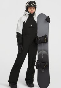 Conjunto de snowboard en blanco y negro con chaqueta de cremallera completa y pantalones a juego. Tabla de snowboard negra con detalles gráficos y fijaciones sujetas.