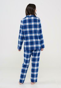 Conjunto de pijama a cuadros azules que incluye una camisa de botones de manga larga y pantalones a juego, confeccionado en una suave tela con una textura ligeramente cepillada.