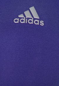 Lila sporttopp i strukturerad tyg, med en silverfärgad adidas-logotyp centrerad på bröstet.