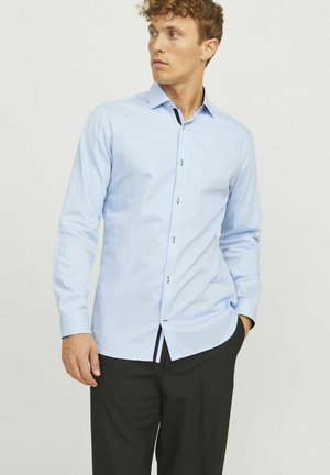 Camicia azzurra chiaro a maniche lunghe, con chiusura a bottoni, texture sottile, accenti neri a contrasto sui bottoni e sull'orlo, vestibilità su misura, abbinata a pantaloni neri.