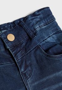 Vaqueros de mezclilla azul oscuro con una textura suave, que presentan un botón de cobre, presillas para cinturón y una cinturilla interior con lunares.