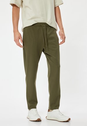 Olivengrønne tapered joggers lavet af blødt stof, med elastisk talje og snøre samt sidelommer. Båret med hvide sneakers.