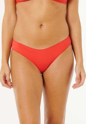 Kobieta w jasnoczerwonych spodenkach bikini i pasującym czerwonym topie bikini, pokazująca tułów od połowy uda do górnej części brzucha.