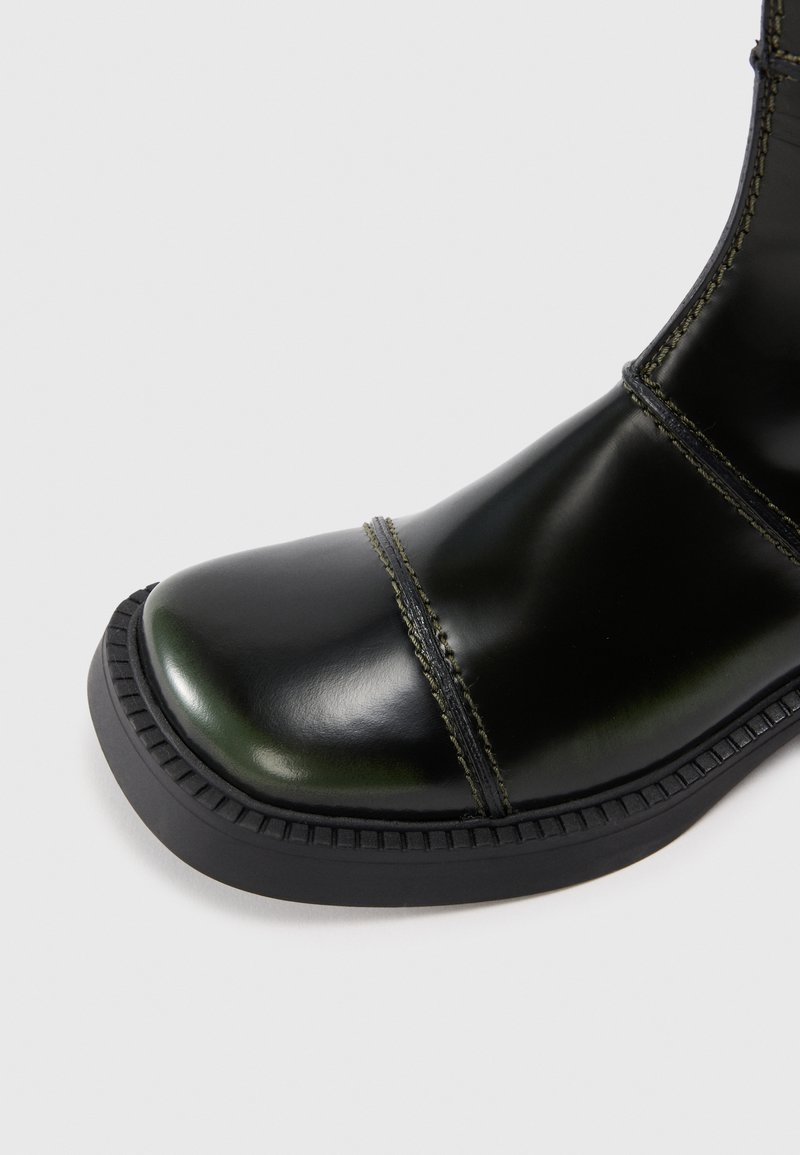 Stivale alla caviglia in pelle nera con punta rotonda, cuciture a contrasto e suola in gomma. Textura liscia con un design moderno.
