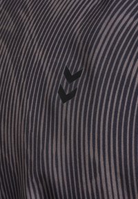 Dunkel gestreifter Stoff mit abwechselnden Marine- und hellen Farbtönen. Linksseitig befindet sich ein schwarzes Logo mit zwei Chevron-Symbolen. Glatte Textur.