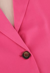 Heldere roze blazer gemaakt van een textuurstof, met een klassiek revers ontwerp en een ronde zwarte knop met de inscriptie "HARPER".