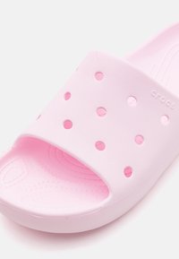 Rozā slip-on kurpe, izgatavota no teksturēta sintētiska materiāla, ar apaļām ventilācijas caurumiem un kontūrveida zolītes dizainu.
