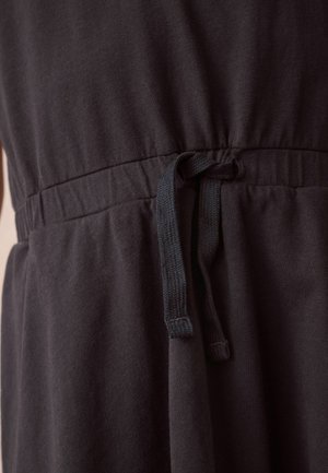 Juodas suknelė su tekstūruotu audiniu, surinkta liemens dalimi ir virvute su audimu. Artimas vaizdas fiksuoja liemens detalę.