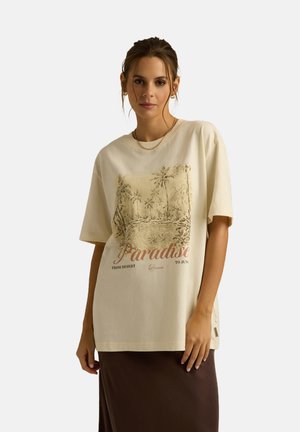 Beżowa bawełniana koszulka z grafiką przedstawiającą palmy i słowo "Paradise" w kontrastującym czerwonym tekście. Krótkie rękawy, luźny krój.