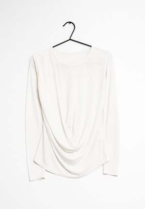 Haut à manches longues drapé en tissu blanc avec un col rond, présentant une texture lisse et des détails de conception subtils le long des côtés.