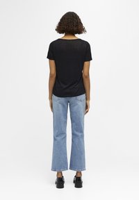 T-shirt noir à manches courtes associé à un jean flare bleu clair, avec un design simple et une coupe légèrement ample. Des chaussures noires chunky complètent le look.