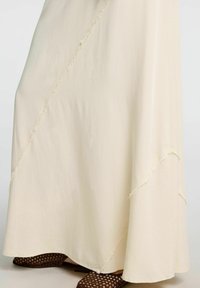 Falda larga de color crema con costuras deshilachadas y un diseño fluido; combinada con zapatos marrones perforados.