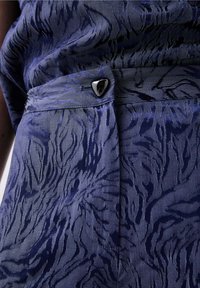 Tissu bleu marine avec texture en relief, présentant un motif en rayures de tigre. Comprend un bouton triangulaire argenté à la taille pour le maintien.