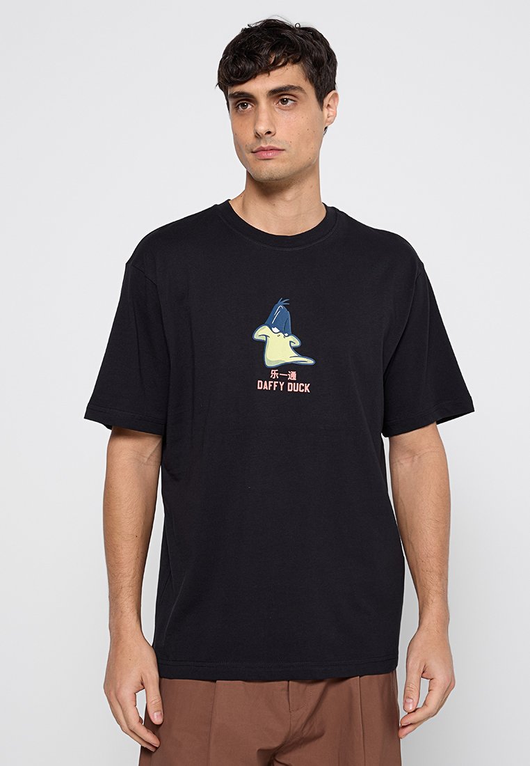 T-shirt en coton noir avec un graphique de Daffy Duck en vert et bleu, accompagné du texte "DAFFY DUCK" en dessous, conçu avec une coupe décontractée.