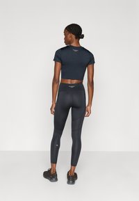 Top deportivo negro recortado con mangas cortas combinado con leggings negros de cintura alta. El conjunto presenta una textura lisa y una marca mínima.