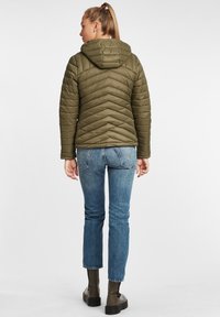 Oliven grønn quiltet jakke med hette, med Chevron-mønster. Kombinert med blå denim jeans og svarte ankel boots.