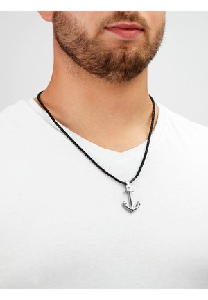 Schwarze geflochtene Halskette mit einem silbernen Ankeranhänger, vor einem schlicht weißen T-Shirt Hintergrund.