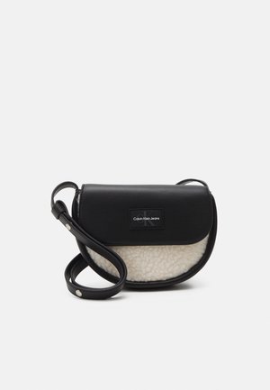 Czarno-biała torba na ramię Calvin Klein z skórzaną klapką, przodem z materiału typu shearling oraz regulowanym paskiem z metalowymi guzikami.