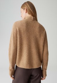Pull en tricot côtelé marron clair avec col montant et manches longues et ajustées, présentant une texture douce et une silhouette décontractée.