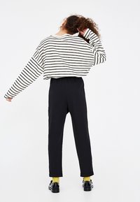 Haut rayé, court, à manches longues en blanc et noir, associé à un pantalon noir taille haute. Comprend des chaussettes jaunes et des chaussures noires.