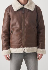 Giacca in pelle marrone con colletto e polsini in pelliccia crema, dotata di una zip frontale e tasche laterali. Finitura texturizzata e design informale.