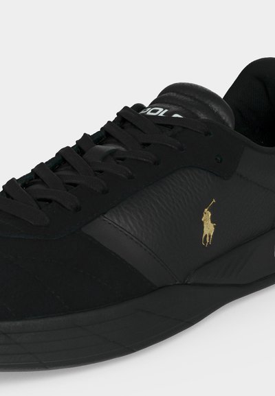 Μαύρο δερμάτινο αθλητικό παπούτσι με μαύρα κορδόνια και χρυσό λογότυπο Polo στη πλευρά, που δείχνει το πάνω μέρος και μέρος της σόλας.