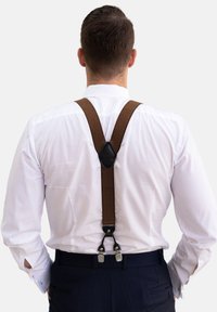 Tirantes de tela marrón con clips de metal, adheridos a una camisa de vestir blanca. Acento de cuero notable y correas ajustables visibles desde la parte trasera.