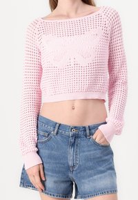 Różowy dzianinowy sweter crop z teksturowanym wzorem i motywem motyla, zestawiony z niebieskimi szortami dżinsowymi. Styl casualowy i dopasowany.