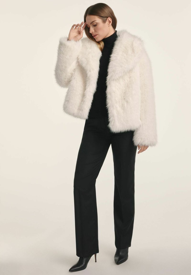 Biała kurtka z sztucznego futra z szerokimi klapami i długimi rękawami, noszona na czarnym golfie. Połączona z czarnymi dopasowanymi spodniami i botkami na obcasie.