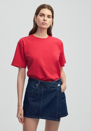 Camiseta de algodón roja con mangas cortas combinada con una minifalda de mezclilla oscura, que cuenta con bolsillos delanteros y un detalle de botón.