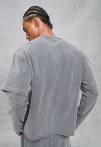 Grijs sweatshirt met lange mouwen, in een relaxed fit en met verlaagde schouders. Zachte, gestructureerde stof met een subtiele vervaagde uitstraling.
