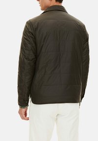 Olive green quilted jacket with a collar, featuring a smooth texture and button details, worn over light-colored pants.