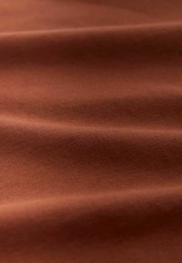 Ruskea kangas, jossa on sileä pinta ja hienovarainen poikkijuova, pehmeitä laskoksia ja lämmin, maanläheinen sävy.