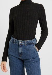 Haut noir côtelé à col roulé avec manches longues, en tissu texturé. Assorti à un jean bleu taille haute avec fermeture par bouton.