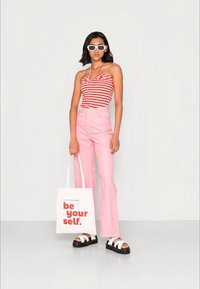 Top de tiras vermelhas e brancas, calças altas rosas, óculos de sol brancos, sandálias pretas de plataforma e uma bolsa branca com texto vermelho.